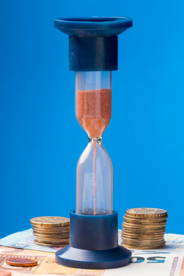 Eine Sanduhr steht auf Geldscheinen auf einem Tisch, als Sinnbild für die Entgeltumwandlung in der betrieblichen Altersvorsorge