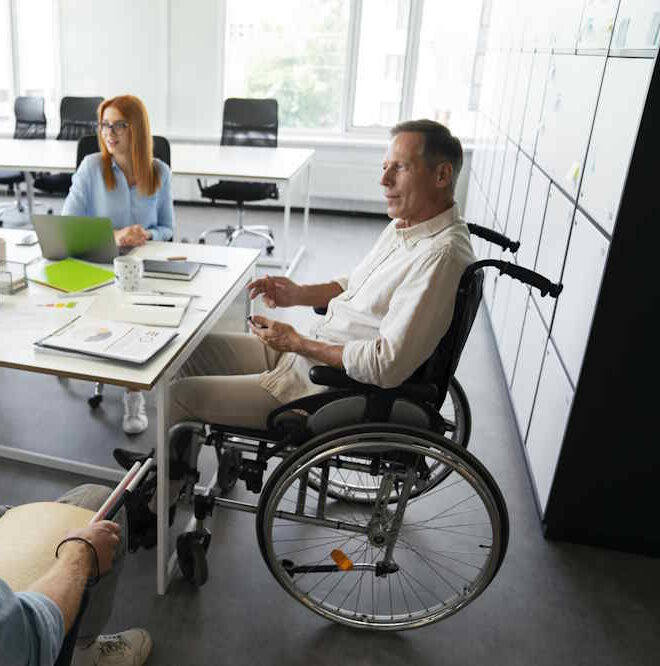 Bild zeigt einen Rollstuhlfahrer, der an einem Bürotisch sitzt. Das steht als Sinnbild für die Grundfähigkeitsversicherung