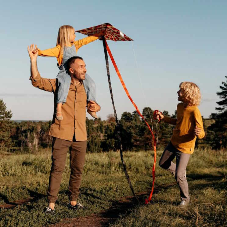 Foto zeigt Vater mit zwei Kindern. Gemeinsam lassen sie einen Drachen steigen. Das steht als Sinnbild für die Freiheit durch die Riester Rente