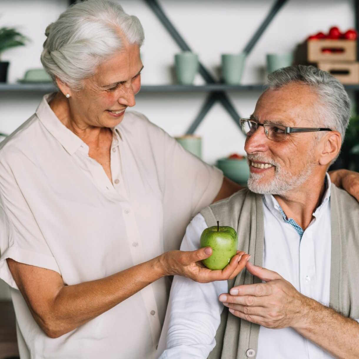 Foto zeigt eine Frau, die einem Mann einen Apfel reicht. Das steht als Sinnbild für die Hilfe im Alter, die man durch eine Rürup Rente erhält.